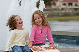 Two small girls sitting at a water fountain laughing
