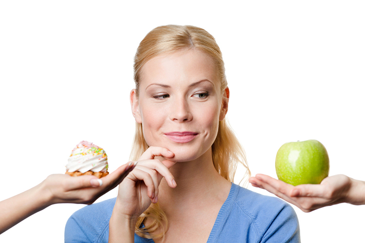 Woman deciding on eating an apple or pastry.