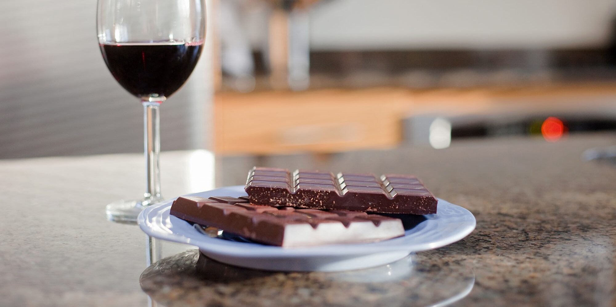 Glass of red wine and dark chocolate on table.