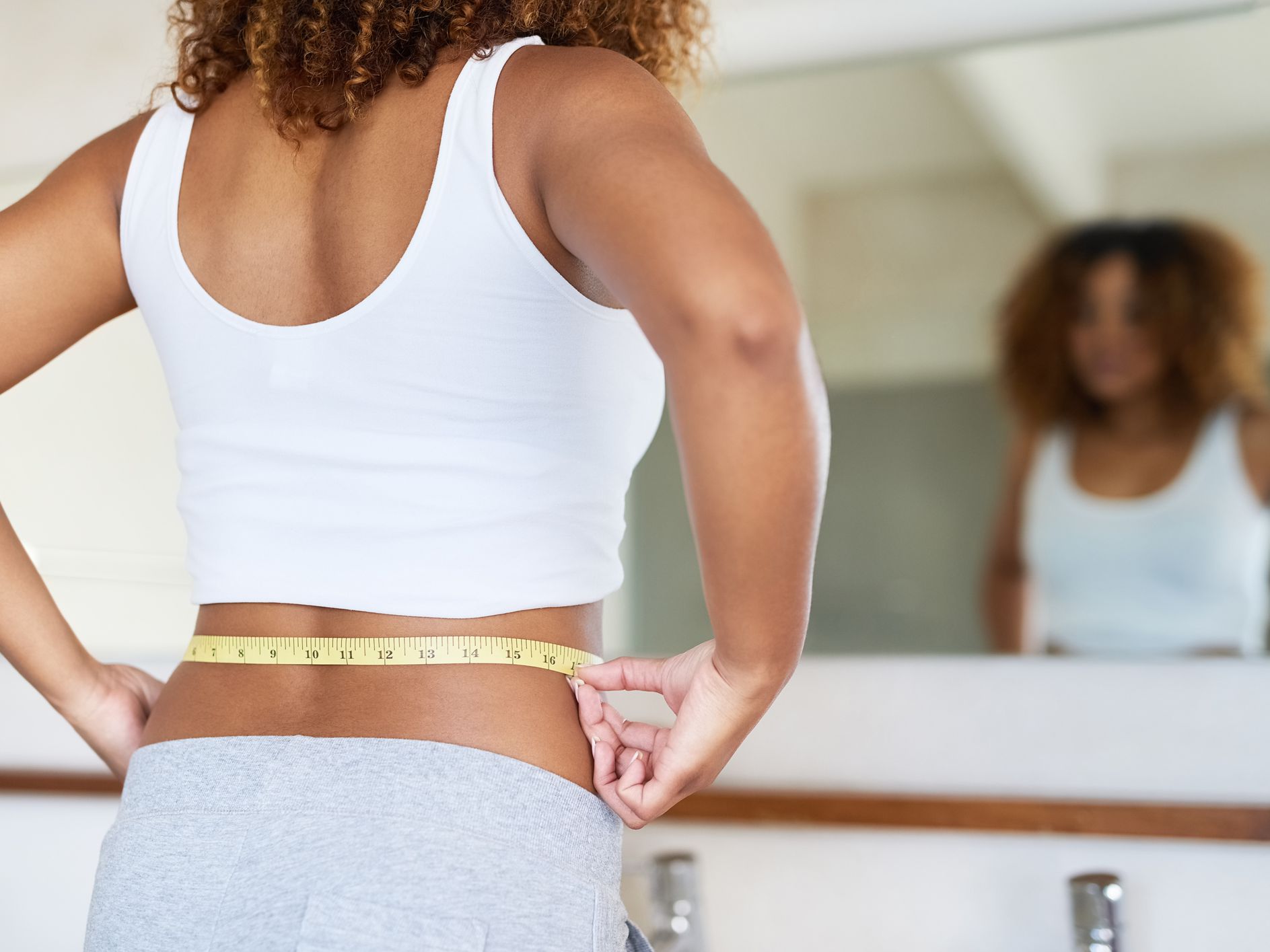 Woman measuring waist in front of mirror.