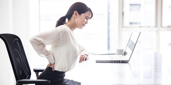 Woman at a desk suffering from chronic back pain.