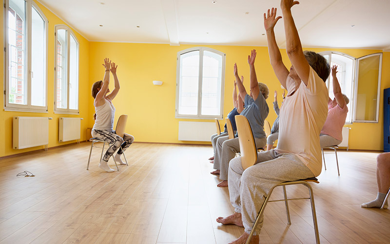 Teacher and active senior women yoga class on chairs